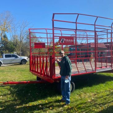 Man standing beside a red trailer in a grassy yard.
