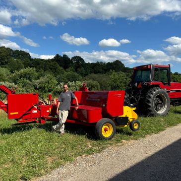 Man standing by red farming equipment and a tractor in a field.