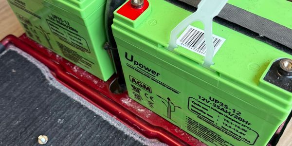 Two green UPower 12V batteries installed on a red platform with screws nearby.