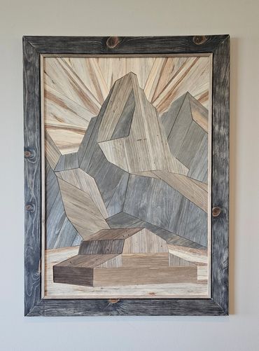 Wooden framed geometric mountain art with sun rays.