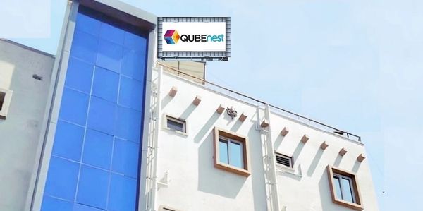 Modern office building with blue glass facade and QUBEnest logo.