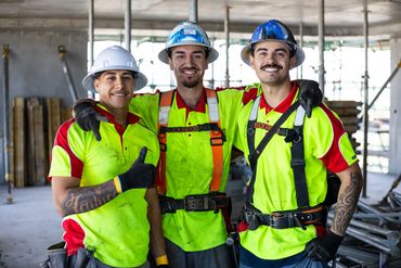 Three construction workers smiling and posing together at a work site.