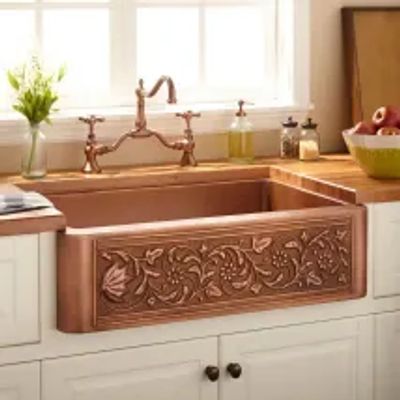 Copper kitchen sink with intricate floral design.