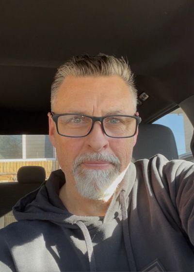 Man with glasses and gray beard inside a car, sunlight on his face.
