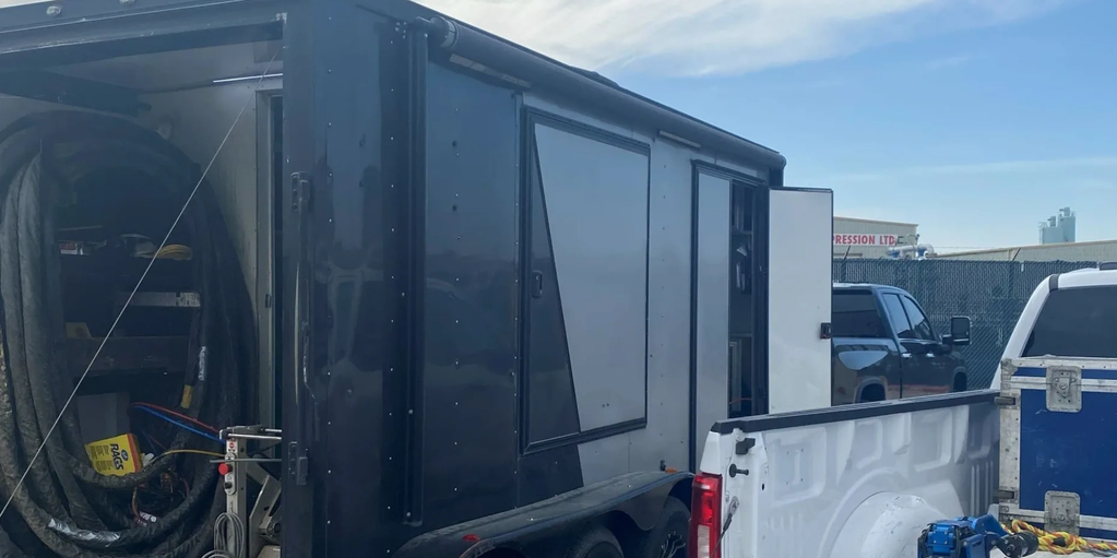 Black utility trailer attached to a white pickup truck in an industrial area.