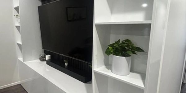 Modern white entertainment unit with TV and shelves, decorated with small plants.