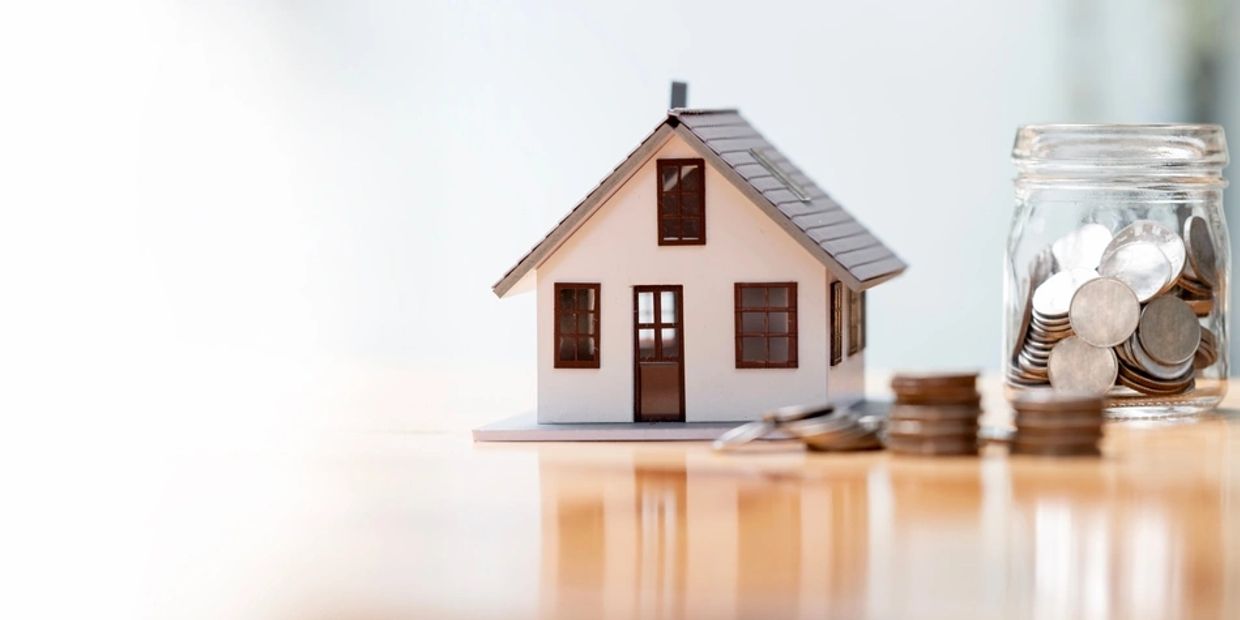 Model house with coins and jar symbolizing real estate investment.