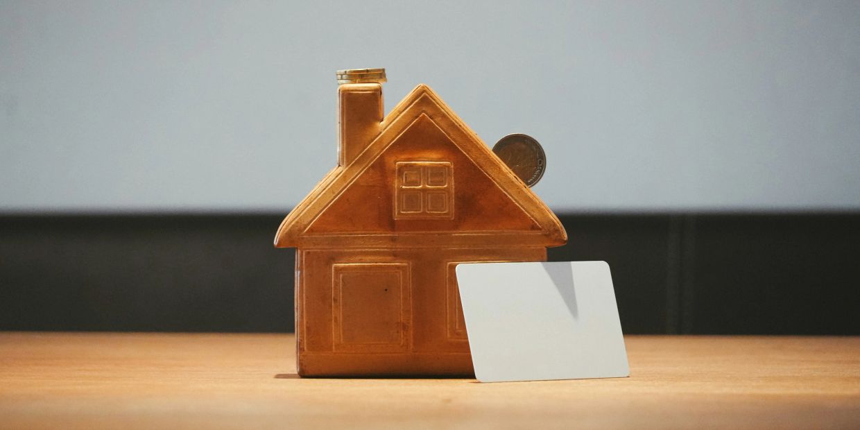 A golden house-shaped piggy bank with a blank card beside it on a wooden surface.