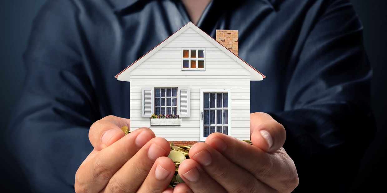 Hands holding a miniature house and gold coins, symbolizing home investment.