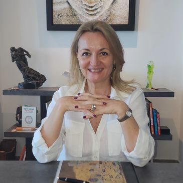 Femme souriante assise à une table avec des mains croisées.