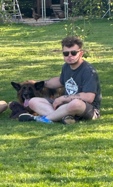 Man with sunglasses sitting on grass with a dog.