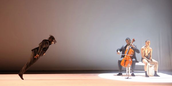 A dancer leaning forward dramatically, a cellist playing, and a seated shirtless man in spotlight.