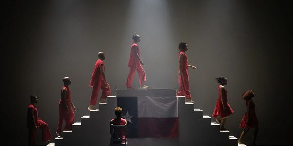 Dancers in red outfits ascending and descending stairs with a Texas flag backdrop.