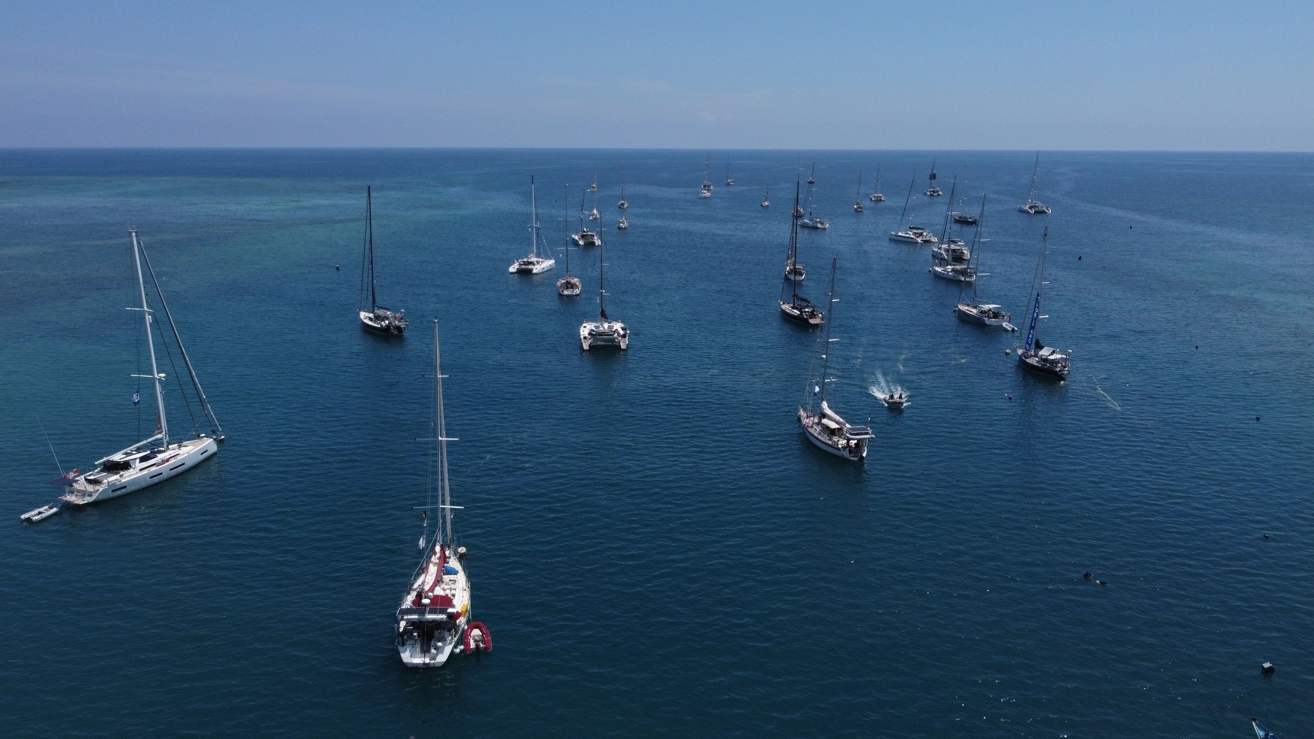 Sailboats anchored on calm blue ocean water under clear sky.