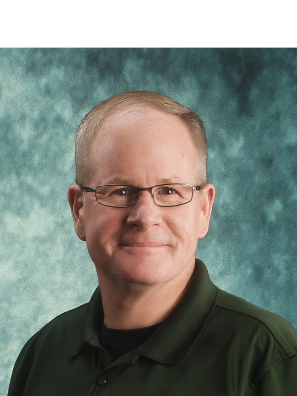 Smiling man with glasses in a green collared shirt against a textured background.