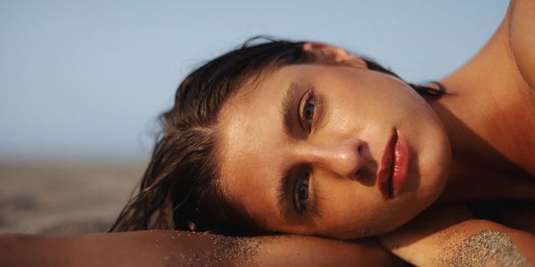 Confident, glowing, radiant woman relaxing on a sandy beach, showcasing beauty and wellness.