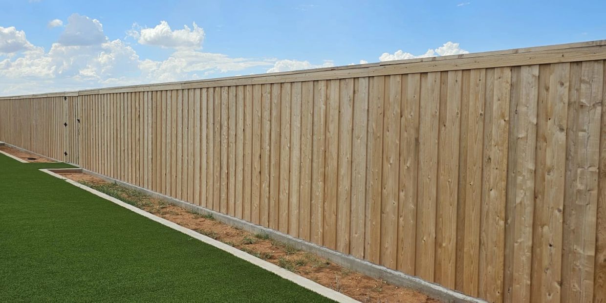 Long wooden fence along a green lawn under a blue sky.