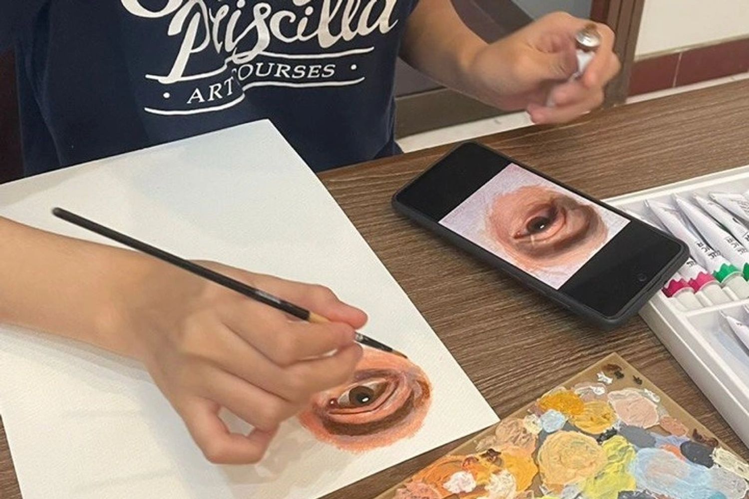 Person painting a realistic eye using a phone reference and a color palette.
