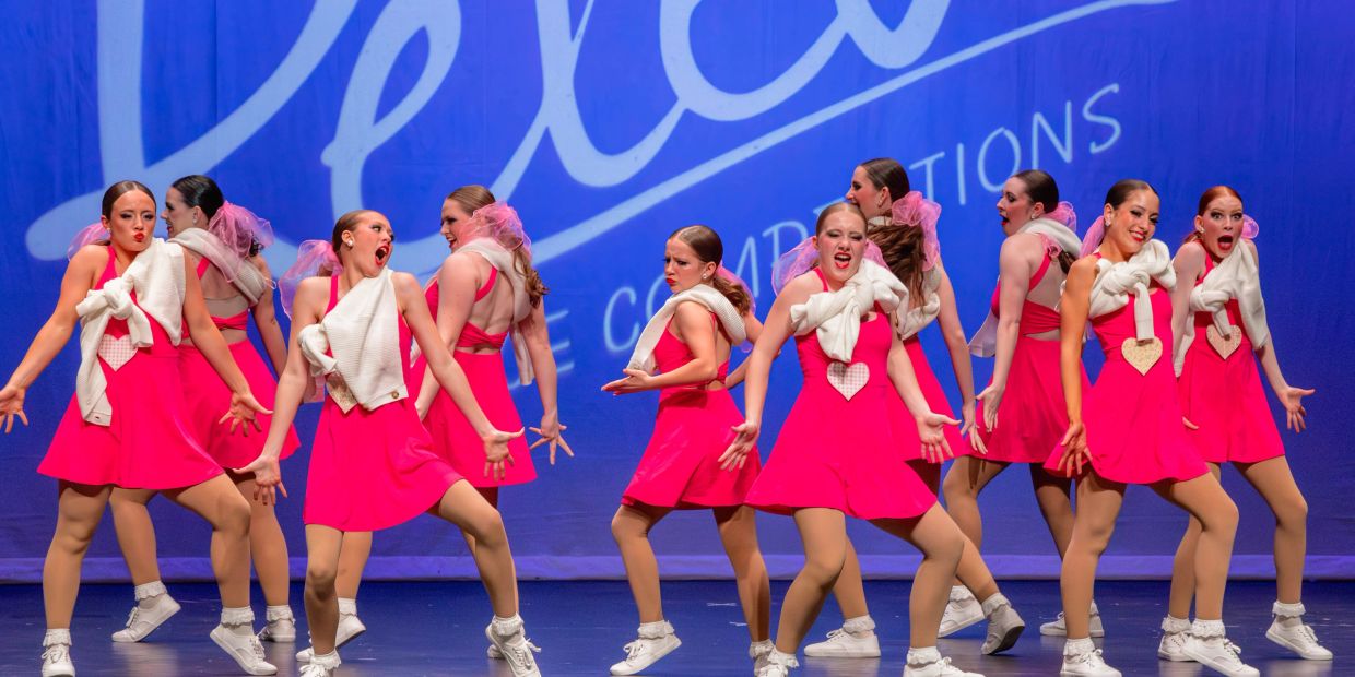 Dancers in pink dresses performing on stage with white sweaters.
