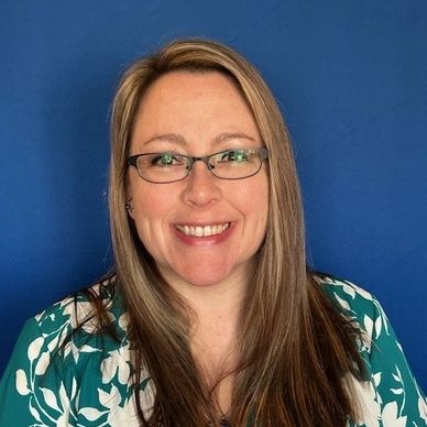 Smiling woman with glasses and floral blouse against a blue background.