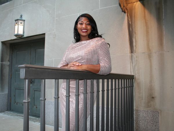 A woman in a sparkly dress smiles while leaning on a metal railing.