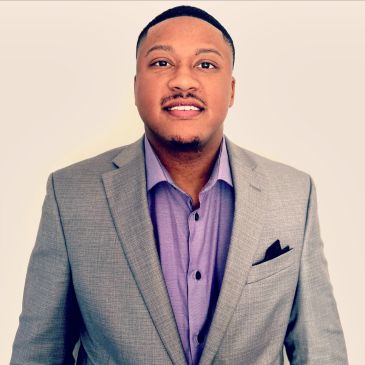 Man in a gray suit and purple shirt smiling.