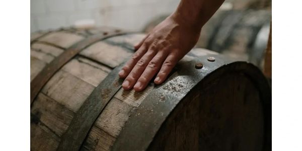 Hand resting on an old wooden barrel with metal bands.