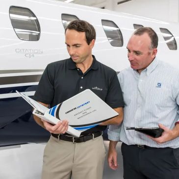 Two men reviewing a Citations CJ4 aircraft manual beside a jet.