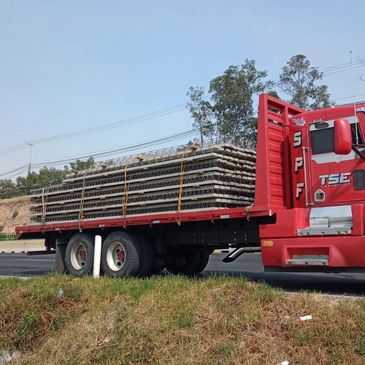 Red truck carrying a large load of stacked metal bars on a highway.