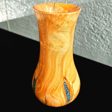 Wooden vase with turquoise inlays on a black surface.