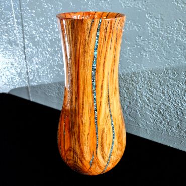 A hand-crafted wooden vase with turquoise inlays on a textured background.