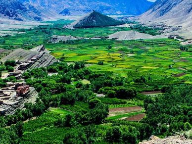 Lush green valley with cultivated fields and mountains in the background.