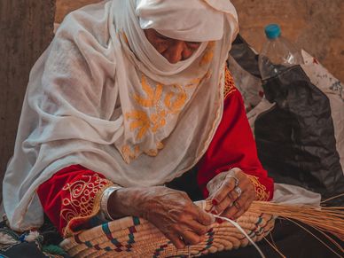 An elderly woman weaving a basket with focused hands.