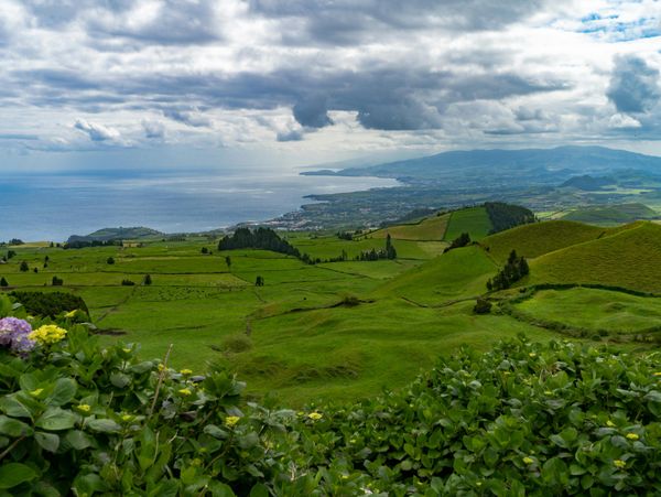 Lush green hills overlooking a cloudy coastline and ocean.
