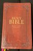 A worn red cover of the Holy Bible with gold embossed text.