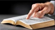 A hand pointing to text in an open book on a table.