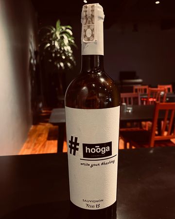 A bottle of Hooga Sauvignon wine on a dark table in a cozy setting.