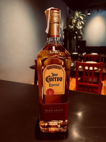 A bottle of Jose Cuervo Especial tequila on a table in a dimly lit room.