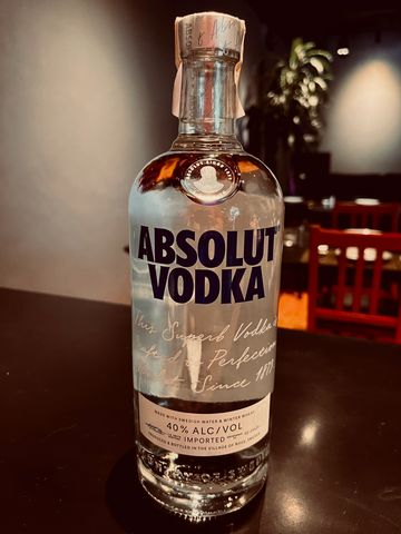 A clear bottle of Absolut Vodka on a dark table with blurred background.