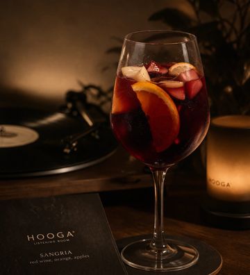 A glass of red sangria with fruit slices on a table in dim lighting.