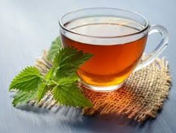 A glass cup of herbal tea with fresh green leaves on a rustic mat.