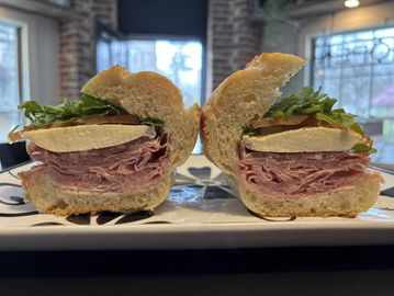 Close-up of a deli sandwich cut in half, showing layers of meat, cheese, and lettuce.