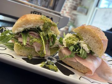 Close-up of a fresh sandwich with ham, arugula, and green pesto sauce.