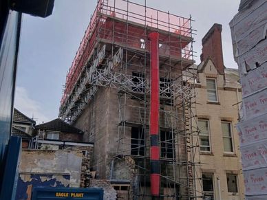 Building under construction with extensive scaffolding and a large red chute.