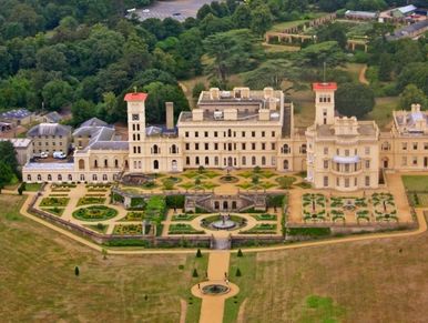 A grand historic mansion with extensive formal gardens and surrounding greenery.