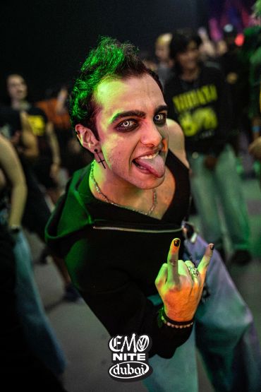 Emo person at a music event making a rock hand sign.