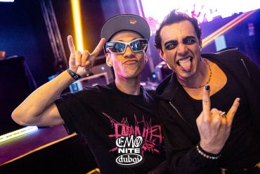 Two men making rock hand signs at a club.
