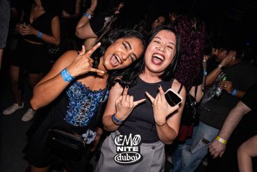 Two women smiling and making rock hand gestures at a party.