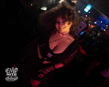 A smiling woman dancing joyfully at a dimly lit club event.
