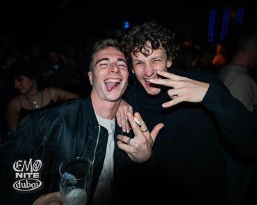 Two young men joyfully posing with hand gestures at a night event in Dubai.